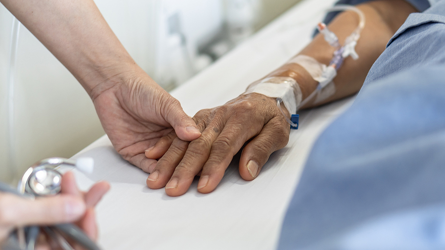 Palliative Care Nurse Practitioner holding the hand of an elderly patient hooked up to IVs.